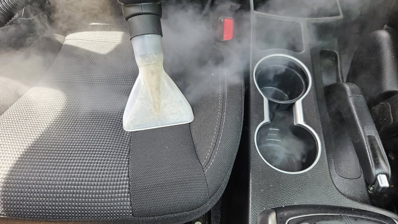 Curățare profesională a tapițeriei auto cu echipament de extracție, pe scaunul din față al mașinii.