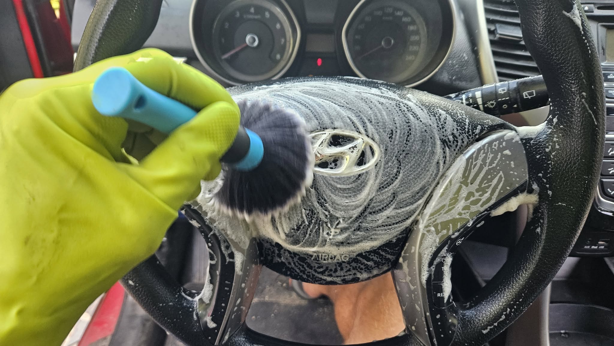Curățarea volanului unui autoturism Hyundai cu spumă și pensulă specială pentru detailing interior.